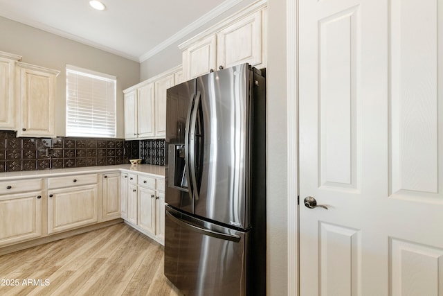 kitchen featuring light wood finished floors, backsplash, stainless steel fridge, crown molding, and light countertops