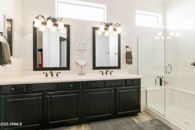 bathroom with double vanity, wood finished floors, a stall shower, and a sink