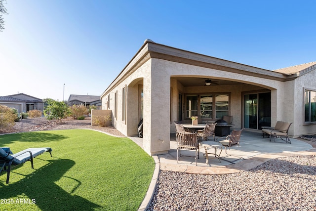 rear view of house with stucco siding, a patio, a lawn, and a ceiling fan