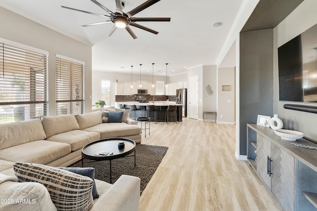 living area featuring ceiling fan, baseboards, ornamental molding, and light wood finished floors