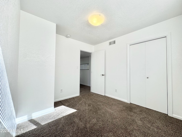 unfurnished bedroom with a closet, a textured ceiling, and dark colored carpet