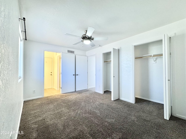 unfurnished bedroom with ceiling fan, dark carpet, and two closets