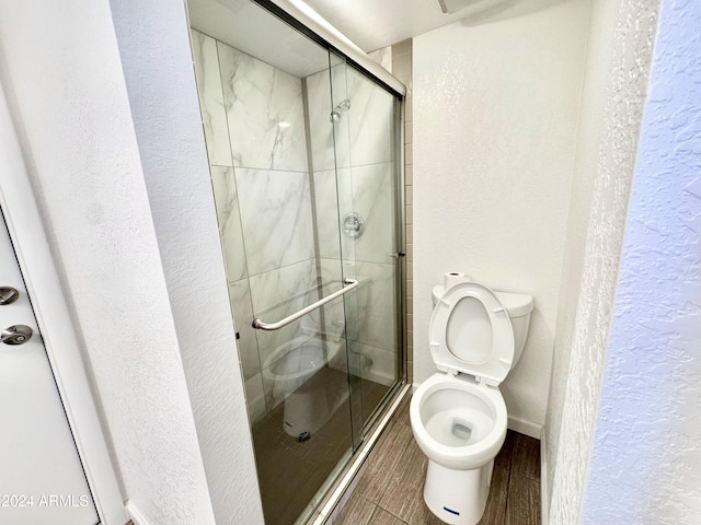 bathroom with hardwood / wood-style floors, a shower with door, and toilet