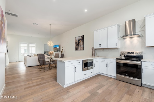 kitchen with white cabinets, kitchen peninsula, stainless steel appliances, and wall chimney range hood