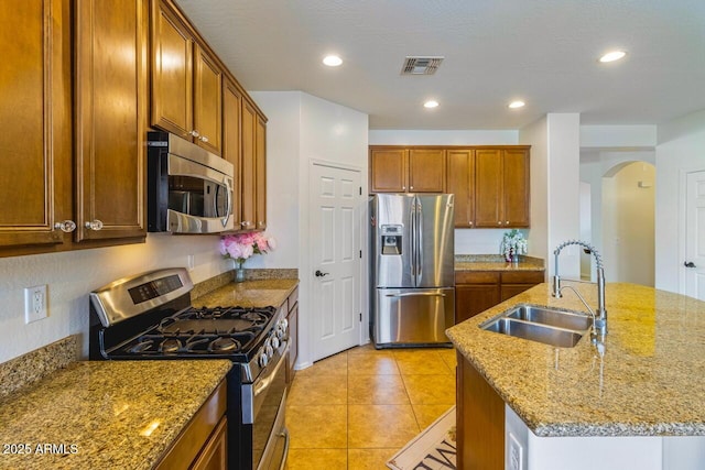 16559 W Lincoln St, Goodyear, AZ 85338 - kitchen featuring stainless steel appliances, arched walkways, light stone countertops, brown cabinets, and recessed lighting