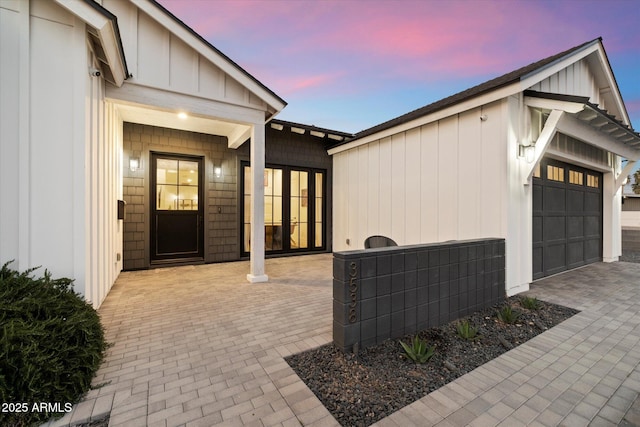 view of exterior entry featuring a garage, decorative driveway, and board and batten siding