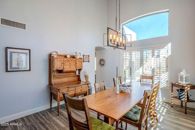 dining room with a notable chandelier, wood-type flooring, and a high ceiling