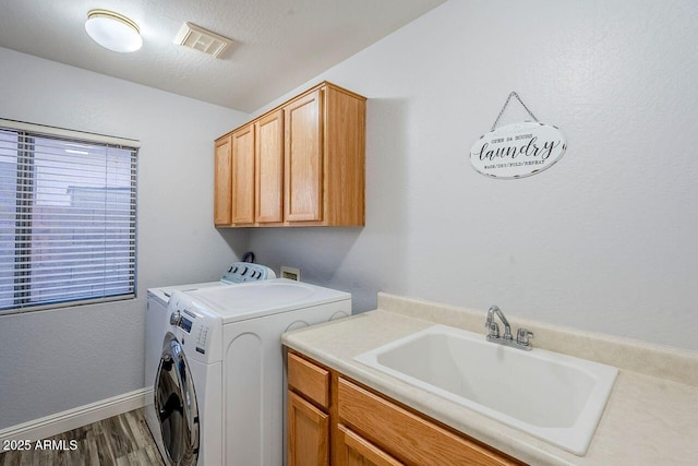 laundry area featuring sink, hardwood / wood-style floors, washing machine and dryer, cabinets, and a textured ceiling