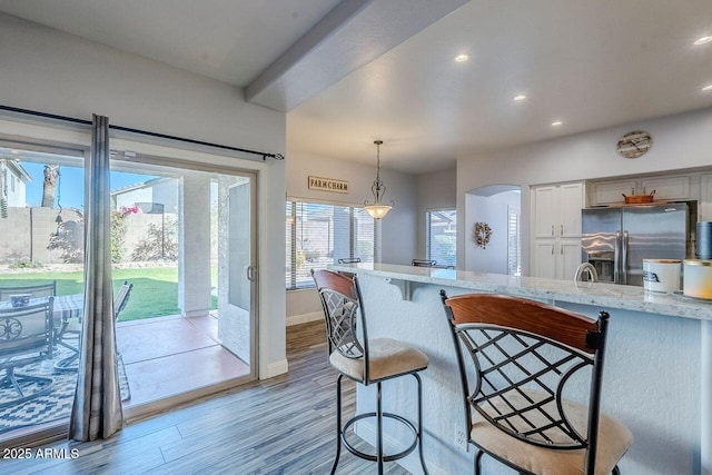 kitchen with light stone countertops, stainless steel refrigerator with ice dispenser, decorative light fixtures, a kitchen breakfast bar, and light hardwood / wood-style flooring