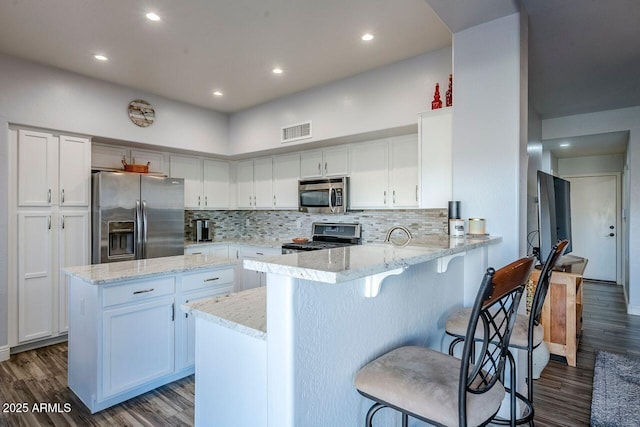 kitchen featuring white cabinetry, light stone countertops, stainless steel appliances, and kitchen peninsula