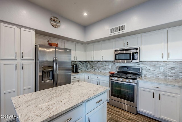 kitchen with tasteful backsplash, appliances with stainless steel finishes, light stone counters, and white cabinets