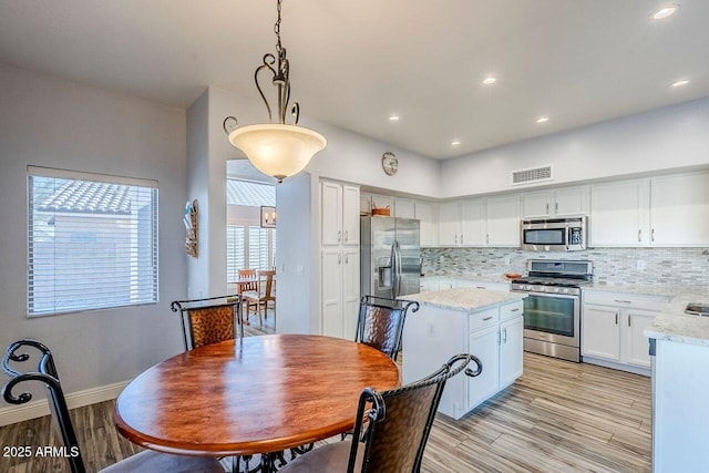 kitchen with stainless steel appliances, white cabinetry, pendant lighting, and backsplash