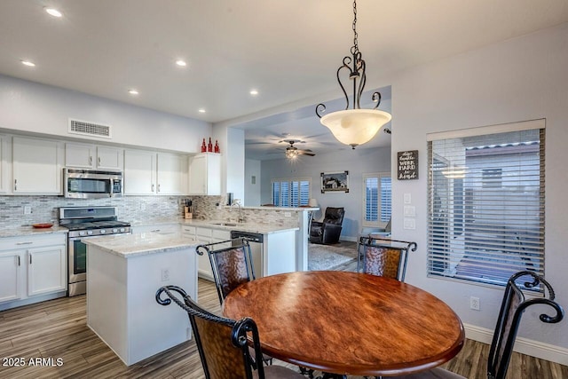 kitchen with pendant lighting, stainless steel appliances, kitchen peninsula, and white cabinets