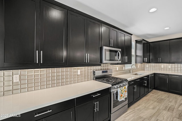 kitchen featuring backsplash, dark cabinets, light countertops, stainless steel appliances, and a sink