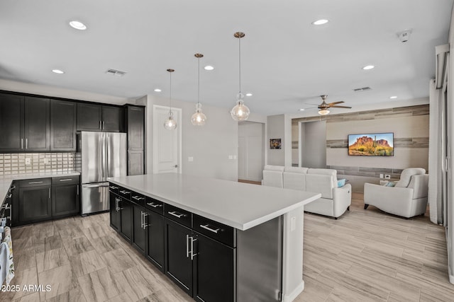 kitchen featuring visible vents, backsplash, ceiling fan, freestanding refrigerator, and dark cabinets