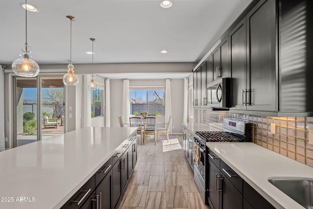 kitchen with decorative backsplash, light countertops, appliances with stainless steel finishes, pendant lighting, and dark cabinets