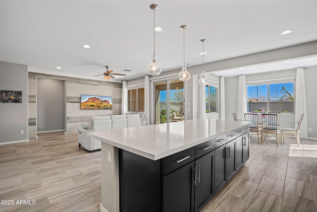 kitchen featuring a ceiling fan, dark cabinetry, a center island, light countertops, and hanging light fixtures