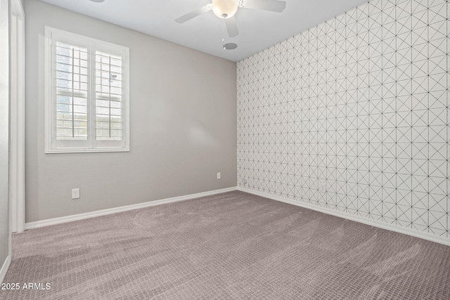 empty room featuring dark colored carpet, baseboards, ceiling fan, and an accent wall