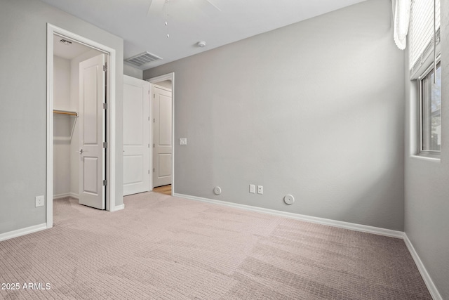 unfurnished bedroom with a spacious closet, visible vents, light colored carpet, and baseboards