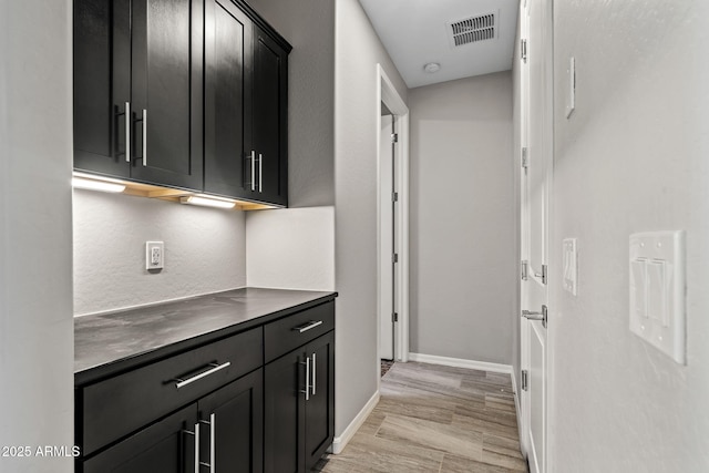 corridor featuring baseboards, visible vents, and light wood finished floors