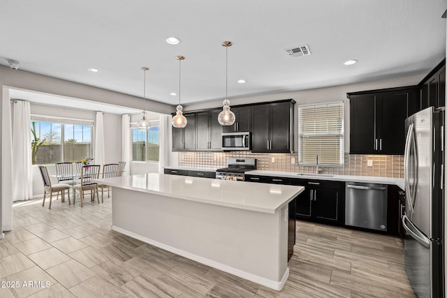 kitchen featuring visible vents, a sink, a center island, appliances with stainless steel finishes, and light countertops