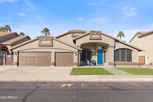 mediterranean / spanish house with a garage, a tiled roof, concrete driveway, and stucco siding
