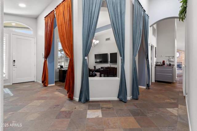 entrance foyer with arched walkways, stone finish floor, visible vents, and baseboards