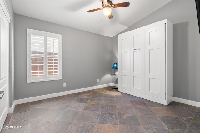 unfurnished bedroom with vaulted ceiling, stone finish floor, a ceiling fan, and baseboards