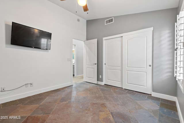 unfurnished bedroom featuring stone tile floors, a closet, visible vents, ceiling fan, and baseboards