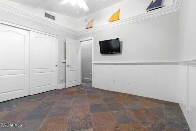 unfurnished bedroom with a wainscoted wall, a closet, stone tile flooring, and visible vents