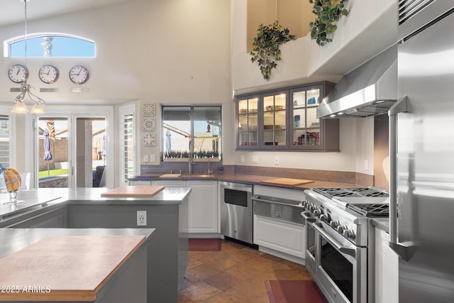kitchen featuring high end appliances, white cabinets, glass insert cabinets, hanging light fixtures, and a sink