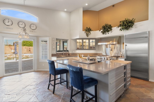 kitchen with high vaulted ceiling, stone tile floors, wall chimney exhaust hood, and high quality appliances