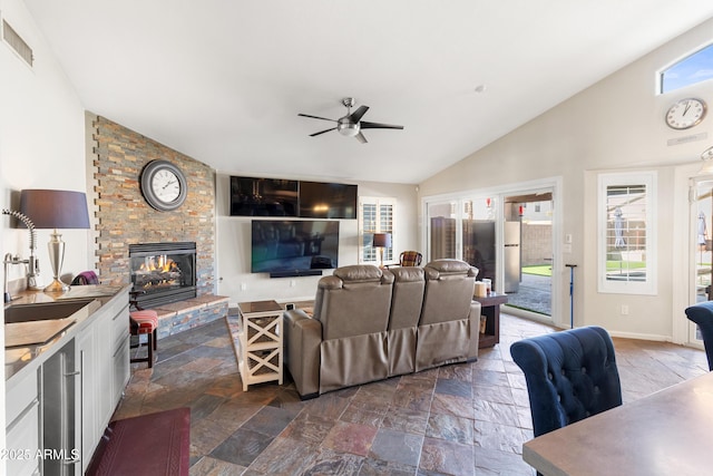 living room with a large fireplace, stone tile floors, visible vents, ceiling fan, and high vaulted ceiling