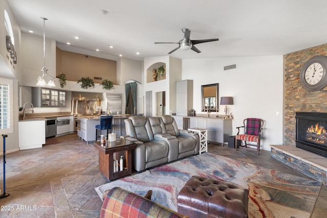 living room with visible vents, a ceiling fan, stone tile flooring, a stone fireplace, and high vaulted ceiling