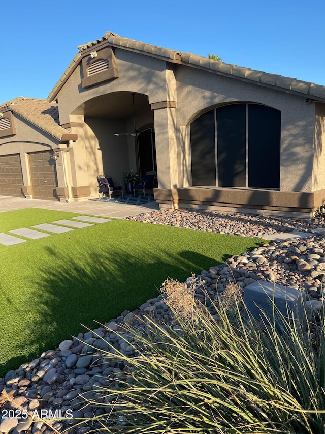 rear view of property featuring a garage, a tiled roof, a lawn, and stucco siding