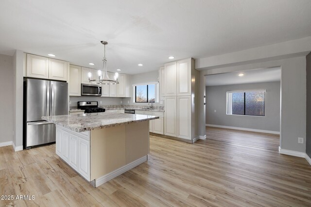 kitchen with light stone counters, a center island, stainless steel appliances, a sink, and light wood-type flooring