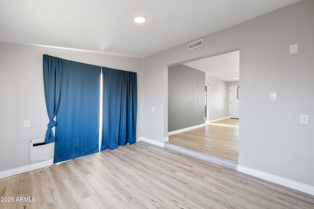 spare room with wood finished floors, visible vents, and baseboards