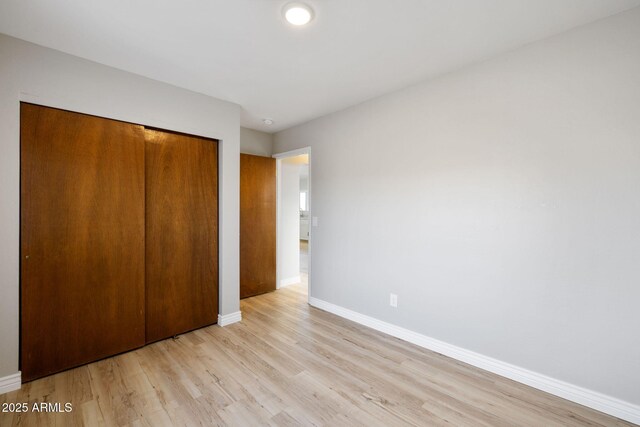 unfurnished bedroom with light wood-style floors, a closet, and baseboards