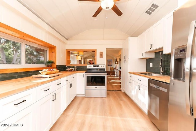 kitchen with vaulted ceiling, appliances with stainless steel finishes, light hardwood / wood-style floors, white cabinetry, and wooden counters