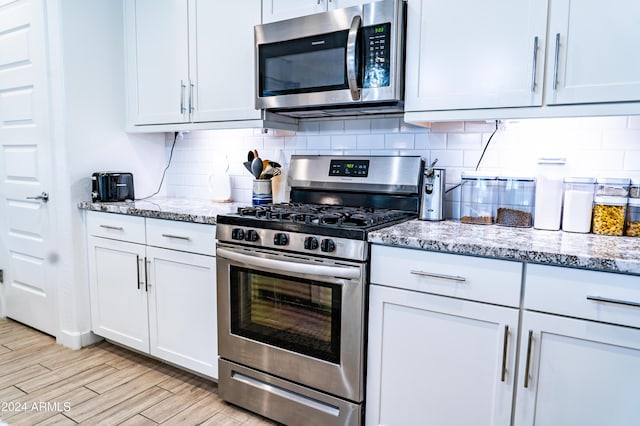 kitchen with tasteful backsplash, light stone counters, stainless steel appliances, light hardwood / wood-style floors, and white cabinetry