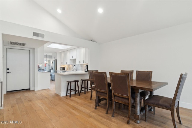 dining room featuring high vaulted ceiling, sink, and light hardwood / wood-style flooring