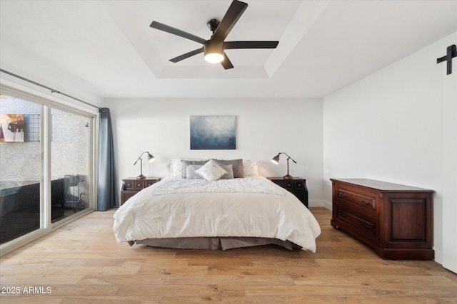 bedroom featuring access to outside, a raised ceiling, ceiling fan, a barn door, and light hardwood / wood-style floors