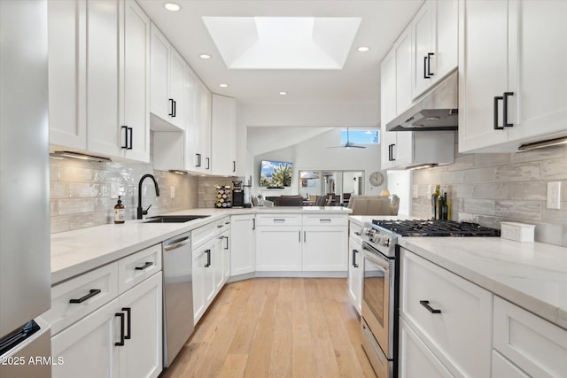 kitchen with sink, appliances with stainless steel finishes, white cabinetry, a skylight, and light wood-type flooring