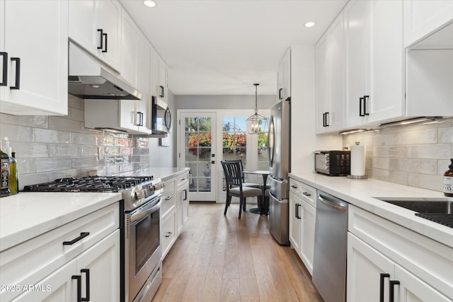 kitchen featuring stainless steel appliances, white cabinetry, hanging light fixtures, and light wood-type flooring