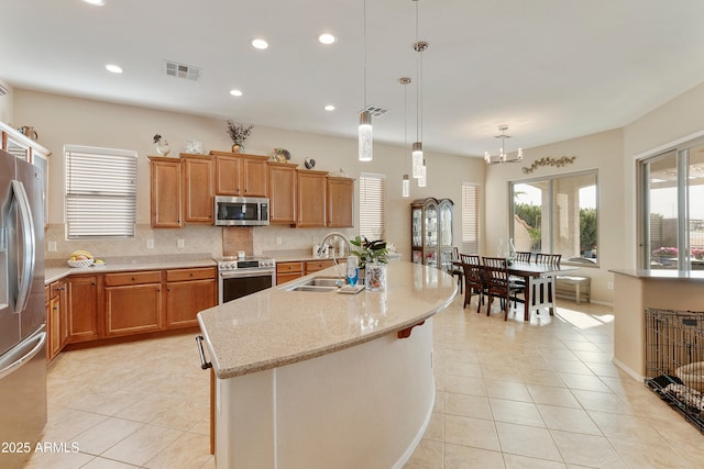 kitchen with sink, tasteful backsplash, decorative light fixtures, stainless steel appliances, and a kitchen island with sink