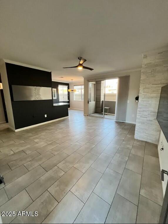 unfurnished living room featuring a healthy amount of sunlight, ceiling fan, and baseboards