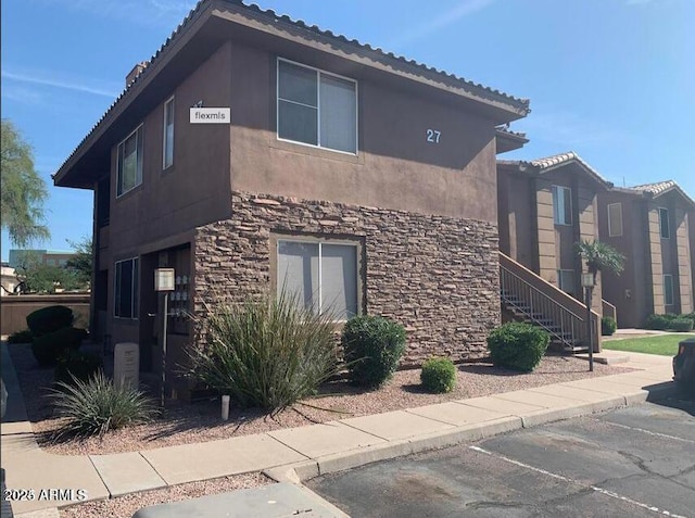 view of side of property featuring stone siding, uncovered parking, and stucco siding