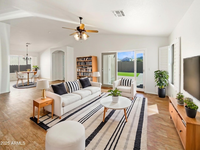 living area with light wood finished floors, visible vents, vaulted ceiling, ceiling fan with notable chandelier, and arched walkways