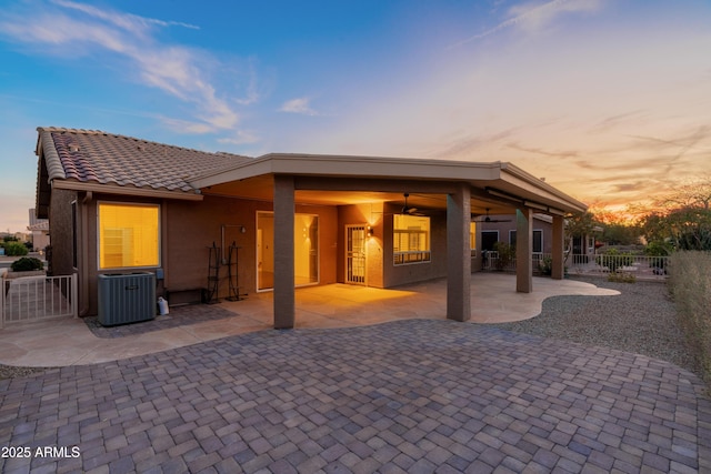 back house at dusk with ceiling fan, central AC unit, and a patio