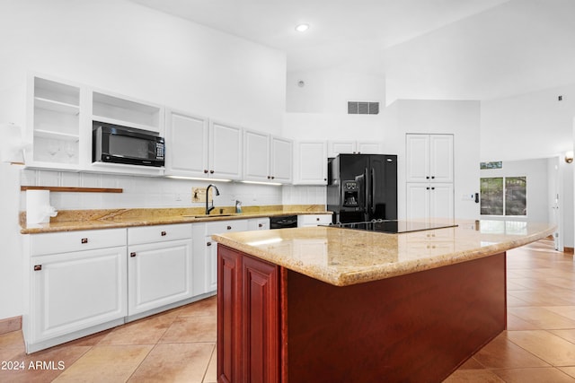 kitchen featuring black appliances, light tile patterned floors, a kitchen island, a towering ceiling, and white cabinets